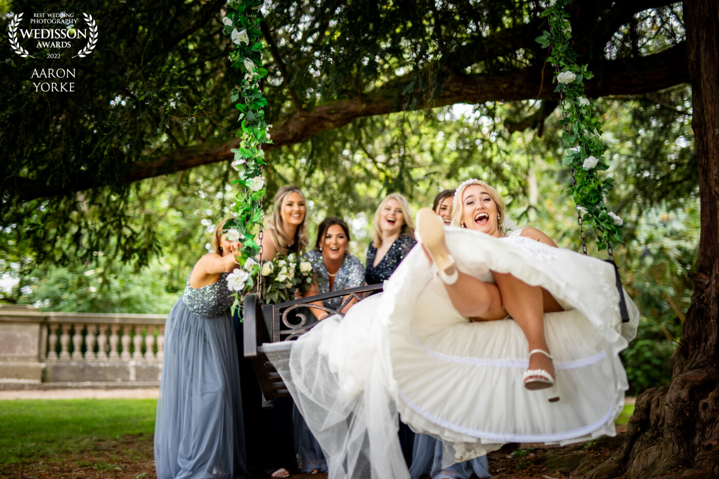 At Wood Norton Wedding Venue in Worcester UK there is an awesome tree swing which is just perfect for nice photographs of newly married couples. In this phot I went for a more fun photo with the bride and her bridesmaids pushing her eon the swing!