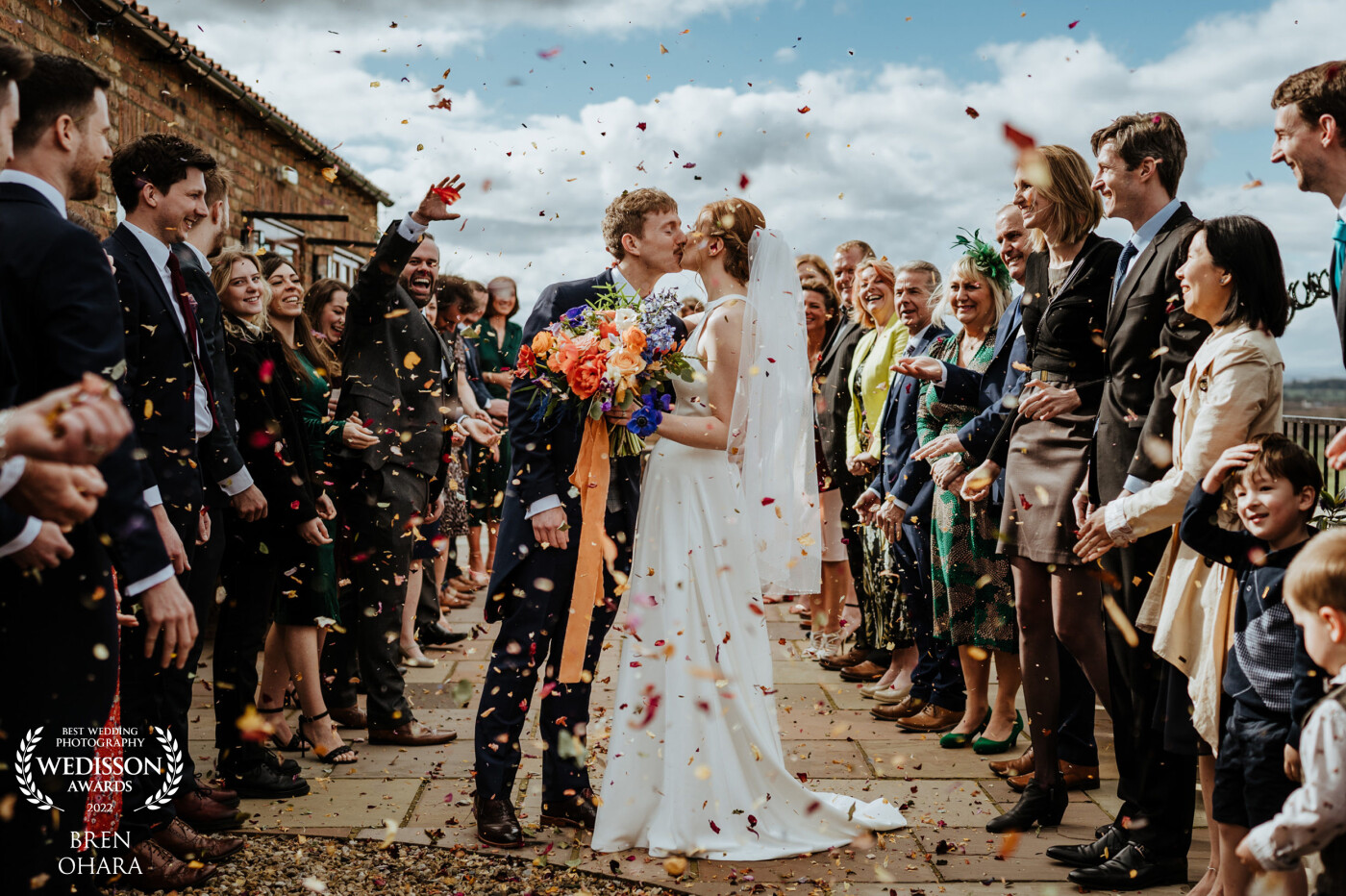 Taken at Thief Hall in North Yorkshire. I asked the couple to stop halfway down the two lines and have a quick kiss. The idea and the photo turned out well. The family had dried flowers for several months to create the lovely confetti.
