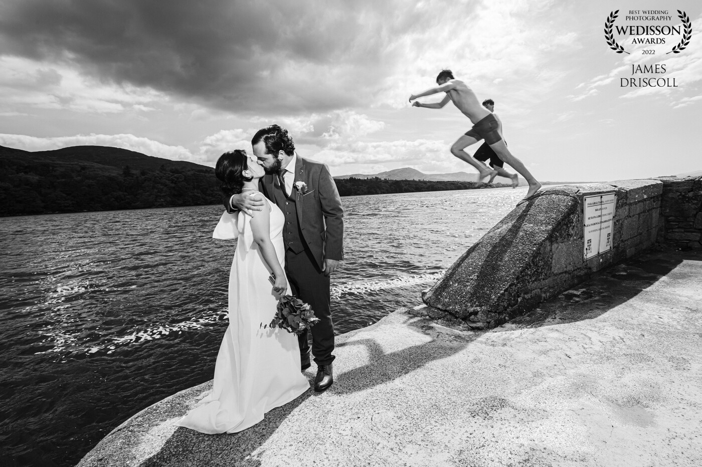 Kenmare Down in the Kingdom of Kerry.<br />
We were walking back to the car when i noticed these kids jumping off the pier.<br />
<br />
Told my couple to wait one second while i ran over to the kids and asked them how would they like to be in a wedding picture. They were well up for it. So i called my couple over and we timed this to perfection as they shared a kiss, the kids leap from the pier,,