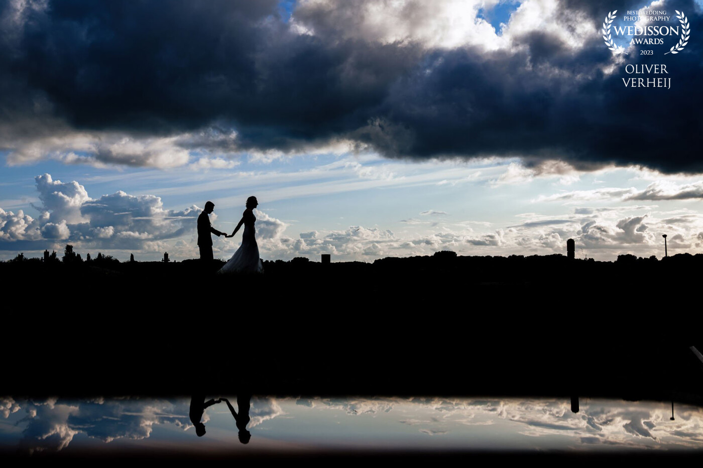 The reflection in the water, the moody clouds and the beautiful couple in this sillhouette make this photo look like a serene painting.