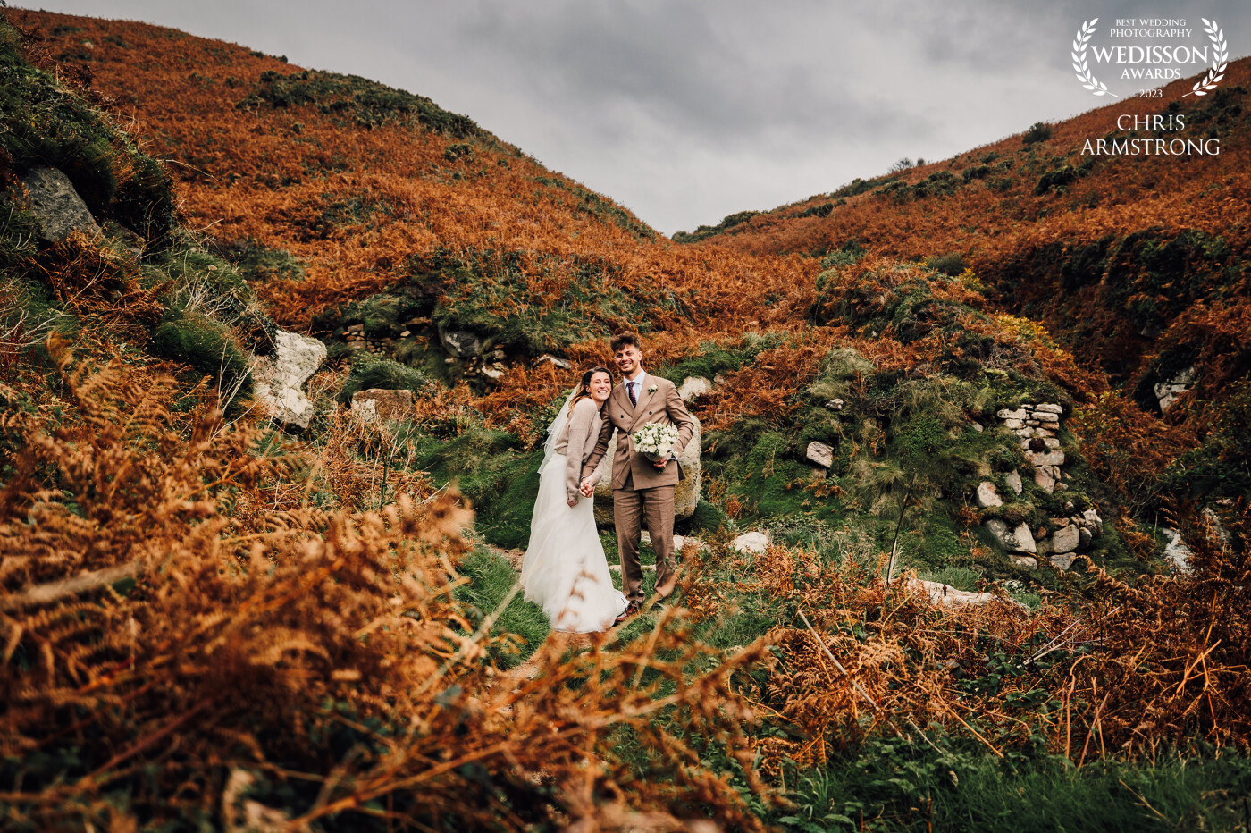 Lauren and Henry surrounded by the burnt orange heather on the cliffs, heading back to theire reception at Chypraze Wedding Barn.