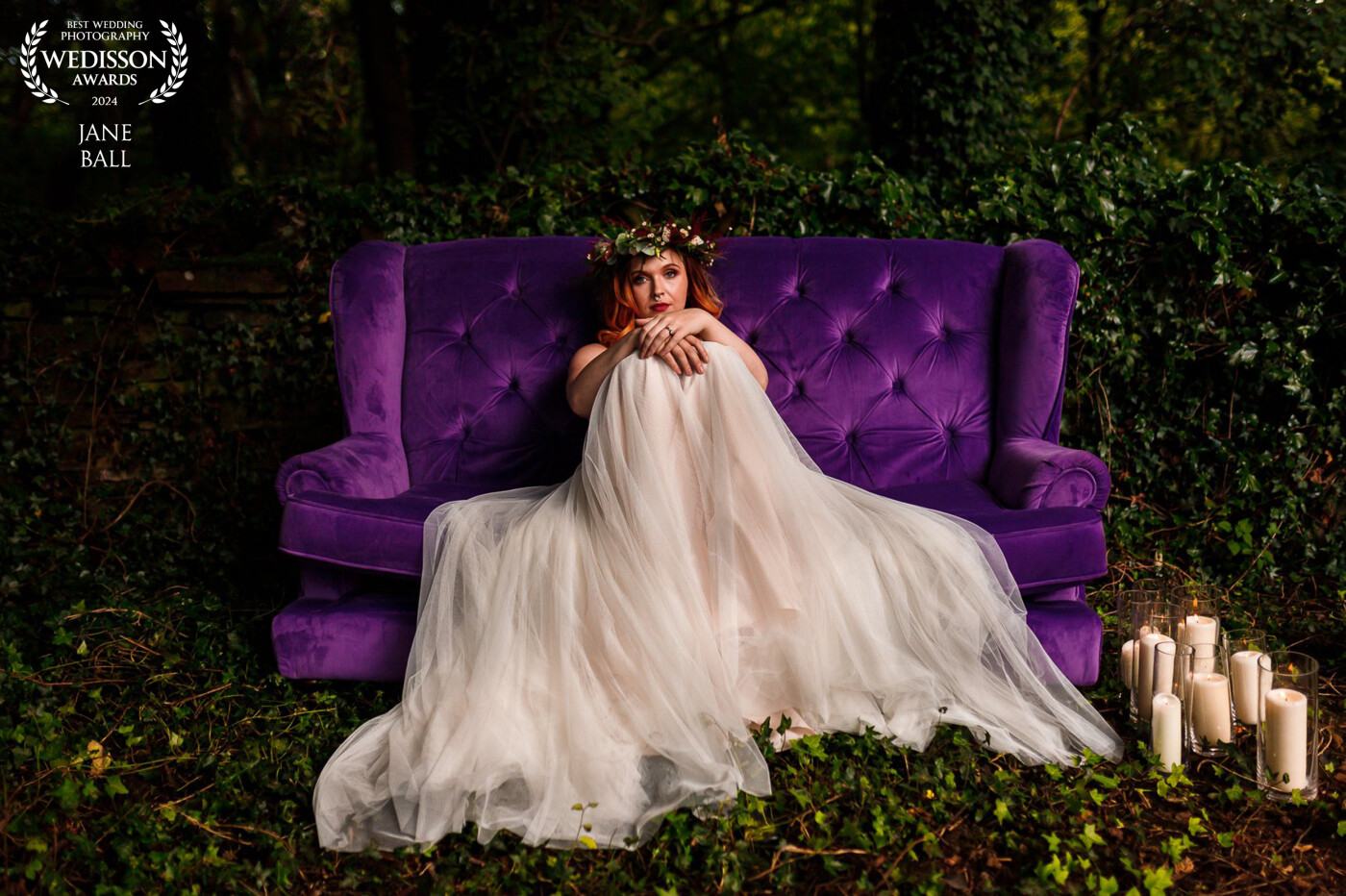 The location for this image is at the back of a rural barn with some beautifully dark and moody woodlands in the background. The venue owner had placed this lush purple sofa in the darkest area so I placed some large candles to one side to counterbalance the dark scene. I asked the bride to sit in the middle of the sofa and we spread her gorgeous boho style dress out and onto the grass. She just "popped" out from the rich colours of the woodland and the sofa. This is one of my most favourite images I've ever produced.