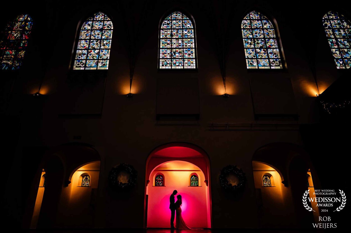 During a beautiful December wedding, we had to move to an indoor location due to the weather to take photos with the bridal couple. Fortunately, we have plenty of those in Venlo. I regularly visit this location to photograph weddings. The light from outside that shines through the stained glass already created a beautiful atmosphere, but adding a little magic completed the image.