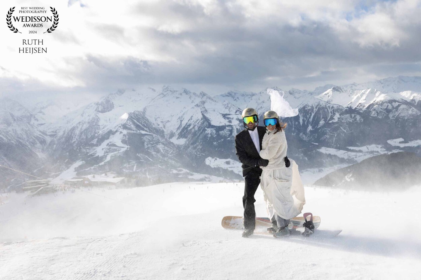 At the pinnacle of love and altitude, the bride and groom embrace each other on their snowboards a the top of this majestic mountain in Austria, overlooking the vast expanse of the Alps. Battling the gusty winds, the snow dances around them, lifting the bride's veil skyward. In this breathtaking moment, amidst the swirling snow, the couple holds tight, savoring not only the thrill of the mountain descent but also the panoramic beauty that love and adventure bring.
