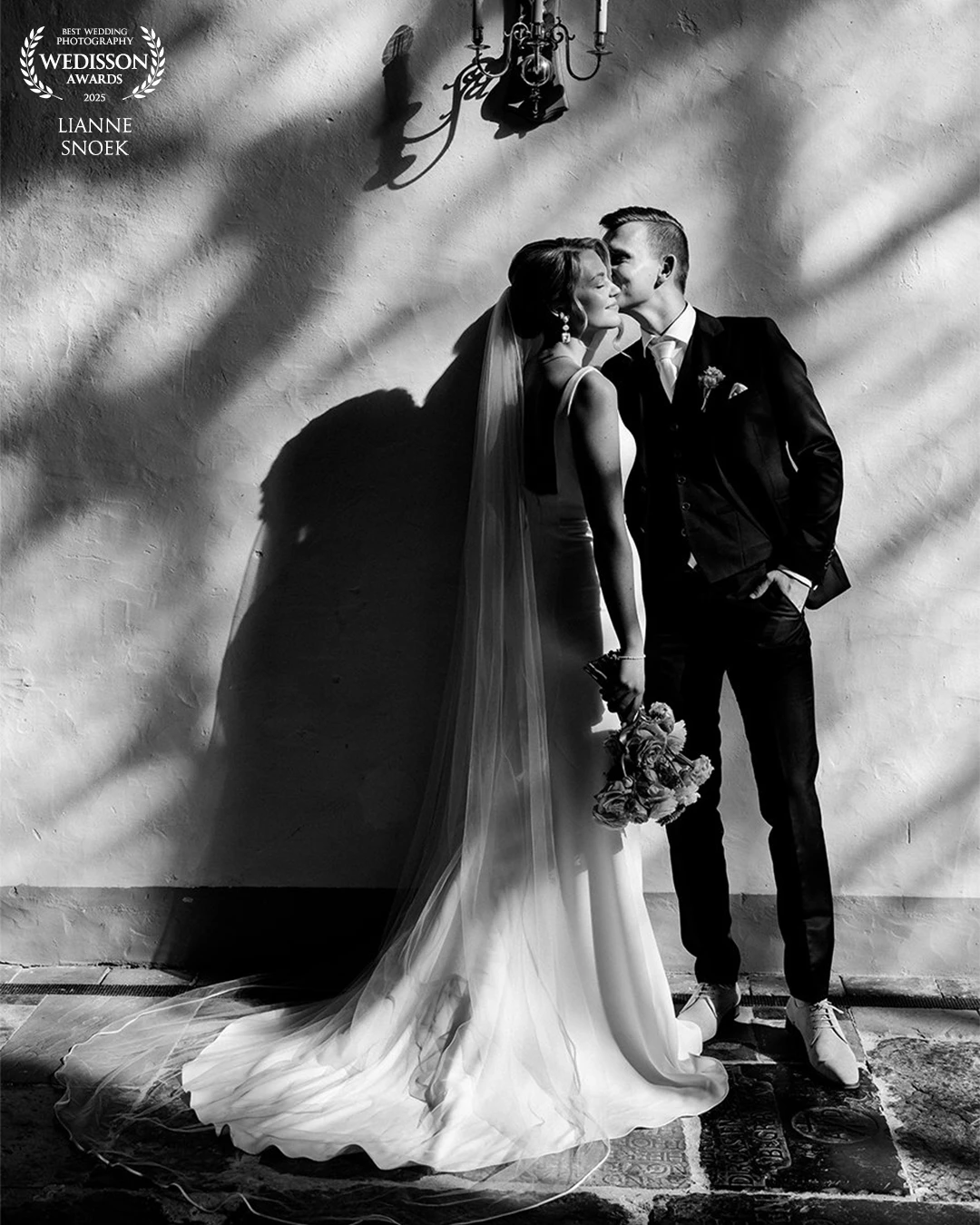A quiet moment in the sunlight through the church-windows . The bride and groom, framed by the beams of sunlight, the shadows create a pattern on the wall.
