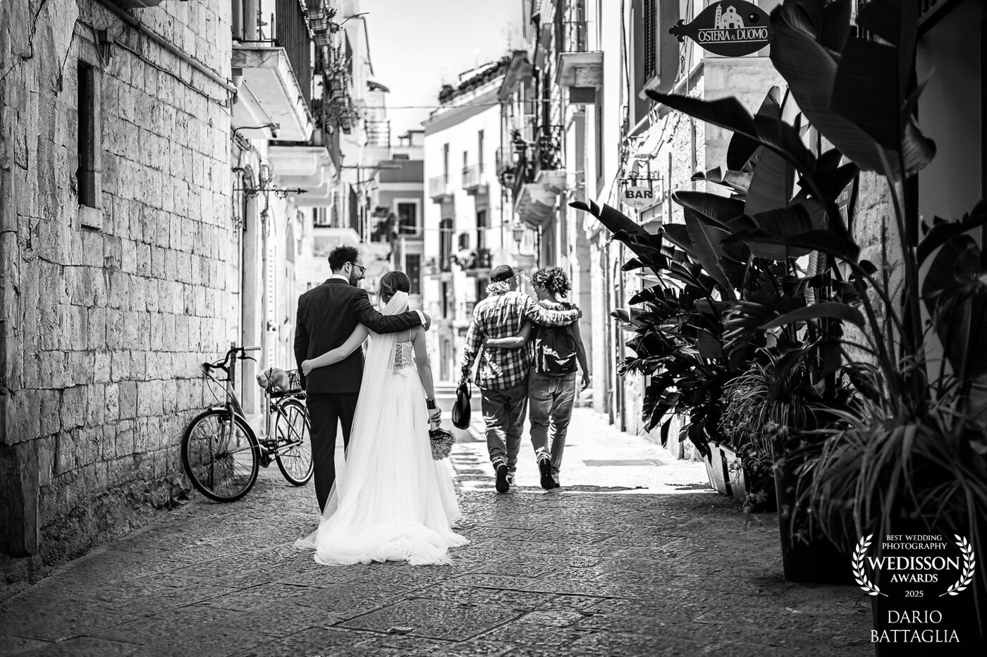 Due mondi che si incrociano.<br />
Gli sposi camminano per la città, vestiti di bianco e di eleganza, mentre davanti a loro una coppia di fidanzati vive la normalità di un giorno qualunque.<br />
È come guardare il presente e il futuro nello stesso istante: da un lato l’inizio di una promessa, dall’altro la sua realizzazione.