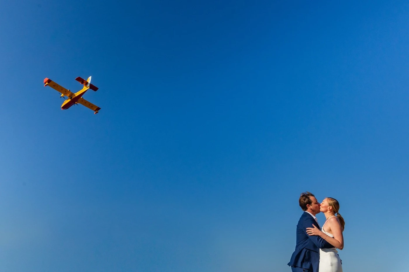 A loving couple under blue skies, a firefighting plane passing overhead.
